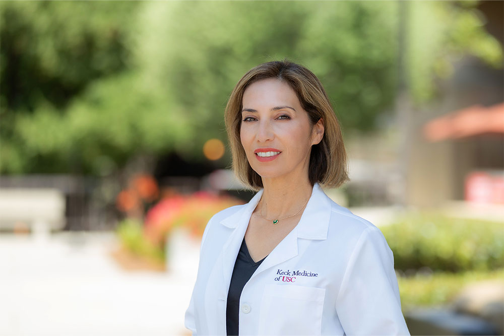Dr. Lilyana Amezcua smiles while standing outside in a white medical coat.