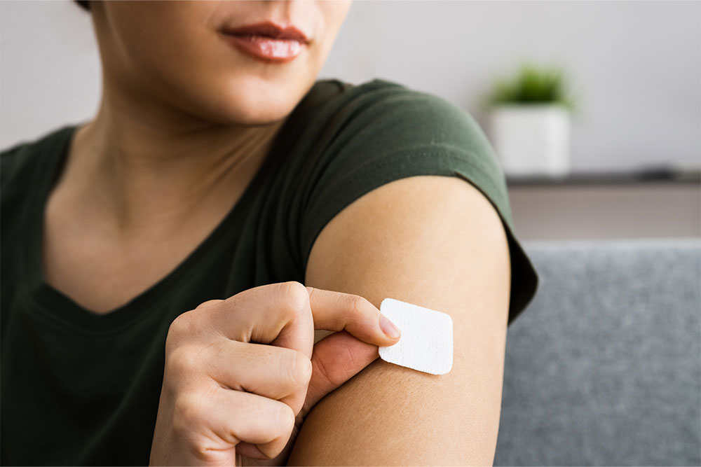 A woman places a hormone replacement therapy patch on her arm.